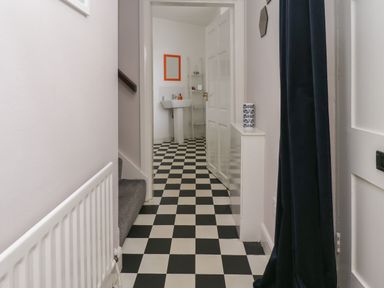 A hallway with black and white checkered floor leading to a bathroom with a pedestal sink and an orange framed mirror at White Feathers in Alnwick