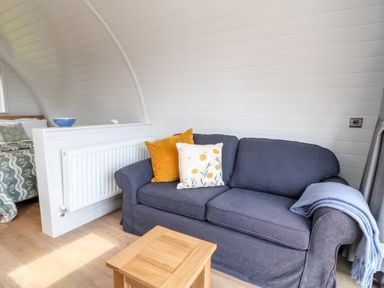 A living area with a blue sofa with cushions and a small wooden table near a bed at Oak in Elmgate near Saltash
