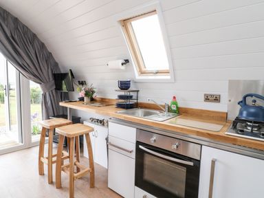 A kitchen with a wooden countertop stools a sink an oven plates a kettle and a window at Oak in Elmgate near Saltash