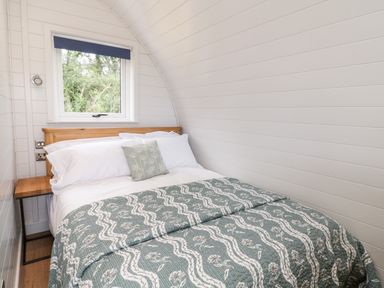 A small bedroom with a double bed a window above the wooden headboard and white paneled walls at Oak Elmgate near Saltash