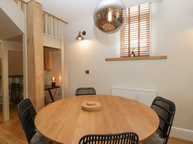 A dining area with a round wooden table black woven chairs a pendant light and a window with wooden blinds at The Old Chapel in Dorstone near Hay-on-Wye