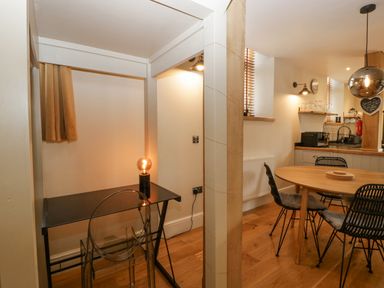 A small workspace with a black desk and lamp next to a dining area with a round wooden table and black chairs at The Old Chapel in Dorstone near Hay-on-Wye