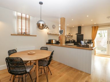 A dining area with a round wooden table and black chairs next to a kitchen with wooden countertops and white cabinets at The Old Chapel in Dorstone near Hay-on-Wye