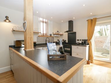A kitchen with a black countertop and wooden shelves near a window and sliding door at The Old Chapel in Dorstone near Hay-on-Wye