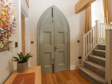 A hallway with an arched double door a staircase with carpet and a table with a plant at The Old Chapel in Dorstone near Hay-on-Wye