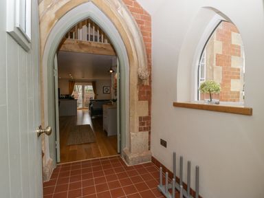 A hallway with an arched doorway leading to a living room with wooden floors and a small window with flowers on the sill at The Old Chapel in Dorstone near Hay-on-Wye