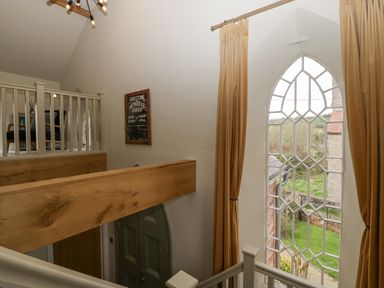 A staircase with wooden beams and a large arched window with curtains at The Old Chapel in Dorstone near Hay-on-Wye