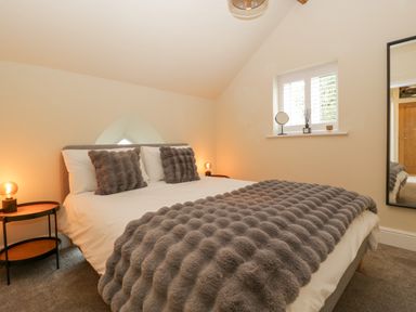 A bedroom with a bed with gray cushions and a blanket two bedside tables with lamps a window and a mirror at The Old Chapel in Dorstone near Hay-on-Wye