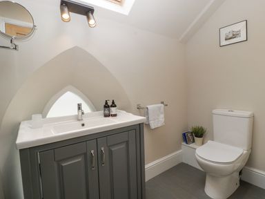 A bathroom with a toilet, grey vanity with sink and toiletries, a towel rack with towel and a framed picture on the wall at The Old Chapel in Dorstone near Hay-on-Wye