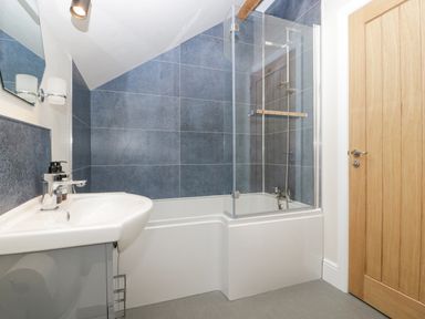 A bathroom with a white bathtub with glass shower screen blue tiled walls a white sink and a wooden door at The Old Chapel in Dorstone near Hay-on-Wye