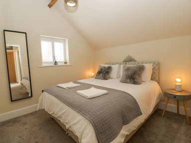 A bedroom with a double bed with gray and white bedding two pillows a mirror on the wall and a side table with a lamp at The Old Chapel in Dorstone near Hay-on-Wye