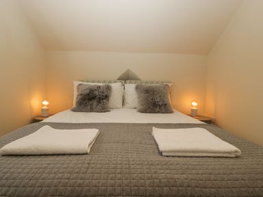 A bed with two gray pillows and two folded towels on a quilted blanket with two bedside tables and lamps at The Old Chapel in Dorstone near Hay-on-Wye