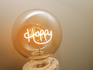 A lit light bulb with the filament spelling the word happy on a stand