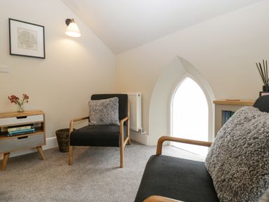 A small sitting area with two black armchairs with wooden frames and gray cushions a wooden side table with books flowers and a basket next to a pointed window at The Old Chapel in Dorstone near Hay-on-Wye