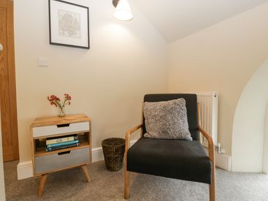 A chair with a cushion next to a small wooden cabinet with books and flowers at The Old Chapel in Dorstone near Hay-on-Wye