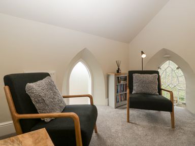 A room with two black armchairs with gray cushions a small bookcase and arched windows at The Old Chapel in Dorstone near Hay-on-Wye