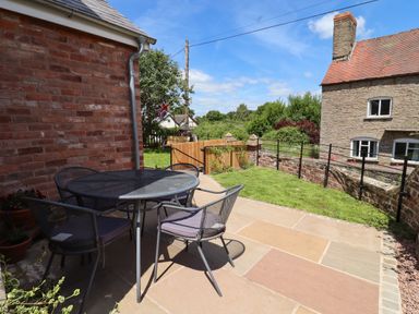 A patio with a black metal table and four chairs next to a brick wall and garden at The Old Chapel in Dorstone near Hay-on-Wye