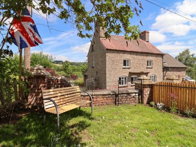 A garden with a wooden bench and a flagpole near a stone house at The Old Chapel in Dorstone near Hay-on-Wye