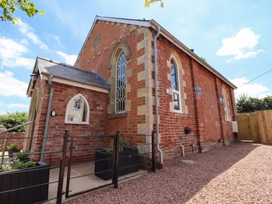 An exterior view of a brick building with arched windows a small fenced area with planters and a gravel pathway at The Old Chapel in Dorstone near Hay-on-Wye