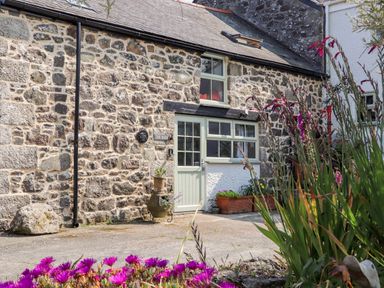 Stone exterior of a building with a pale green door and windows with potted plants and flowers outside at The Barn at Trevothen Farm Coverack