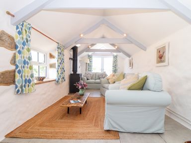 A long living room with sofas coffee table wood burner and curtains at The Barn at Trevothen Farm Coverack