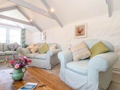 A living room with light blue armchairs and sofas with cushions and a wooden coffee table with flowers at The Barn at Trevothen Farm in Coverack