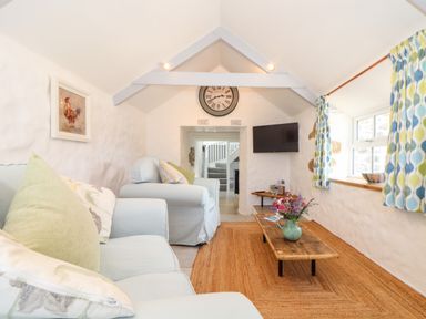A sitting room with light blue sofas a wooden coffee table a wall clock mounted television and patterned curtains at The Barn at Trevothen Farm Coverack