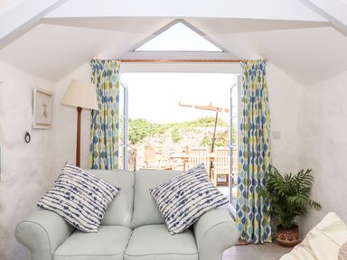 A small living room with a light blue sofa and patterned cushions near an open door leading to a patio at The Barn at Trevothen Farm Coverack