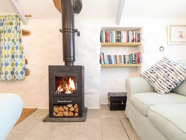 A living room with a wood burning stove firewood sofa with striped pillow bookshelf and patterned curtains at The Barn at Trevothen Farm Coverack