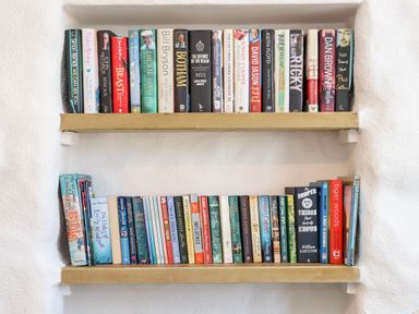 Two wooden shelves filled with books against a white wall at The Barn at Trevothen Farm Coverack
