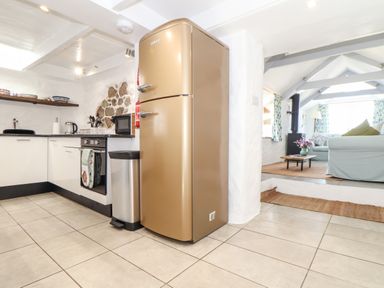 A kitchen with a beige refrigerator next to a stainless steel trash bin and white cabinets at The Barn at Trevothen Farm in Coverack