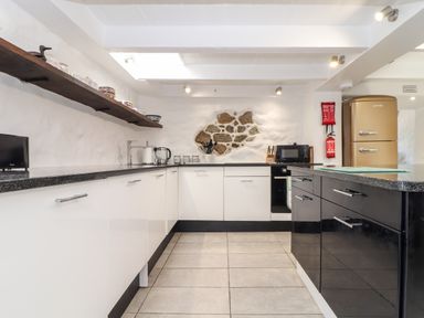A kitchen with white and black cabinets a stone wall feature a beige fridge and appliances at The Barn at Trevothen Farm Coverack