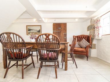 A dining room with wooden chairs a wooden table a leather armchair and a painting on the wall at The Barn at Trevothen Farm Coverack