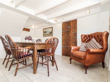 A dining room with a wooden table and chairs and a brown leather armchair at The Barn at Trevothen Farm Coverack