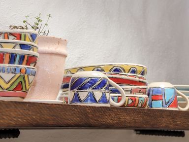 A wooden shelf with colorful patterned bowls and cups and a plant in a terracotta pot at The Barn at Trevothen Farm in Coverack