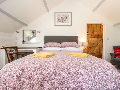 A bedroom with a double bed with patterned bedding and yellow towels two bedside lamps a wooden door a chair and a mirror at The Barn at Trevothen Farm Coverack