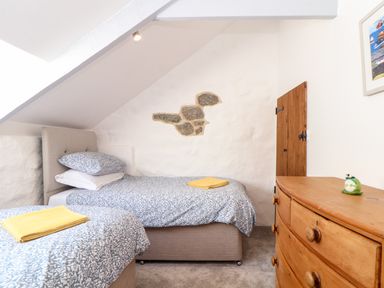 A bedroom with two single beds and a wooden dresser under a slanted ceiling at The Barn at Trevothen Farm Coverack