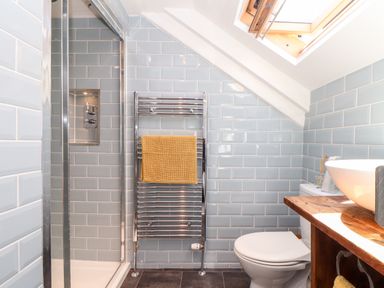 A bathroom with a shower, toilet, wooden counter with a round sink, towel rack with a yellow towel, and skylight window at The Barn at Trevothen Farm Coverack
