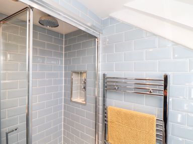A bathroom shower area with light blue subway tiles a glass shower door a recessed shelf a chrome towel rack and a yellow towel at The Barn at Trevothen Farm Coverack