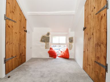 A small room with grey carpet two wooden doors and a window seat with orange cushions at The Barn at Trevothen Farm in Coverack
