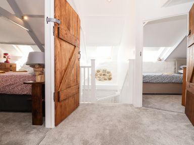 A hallway with carpeted floor and wooden doors leading to two bedrooms at The Barn at Trevothen Farm in Coverack