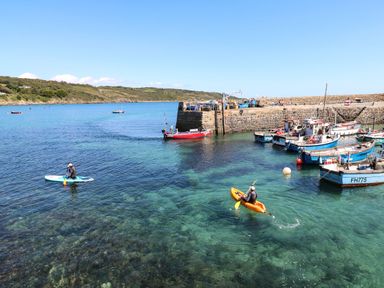 A harbor with boats and people kayaking in clear water at The Barn at Trevothen Farm in Coverack