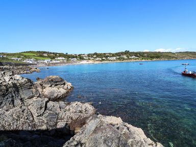 A rocky coastline overlooking a bay with houses and boats on the water at The Barn at Trevothen Farm in Coverack