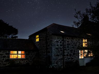 A stone house lit from inside at night with a starry sky in the background at The Barn at Trevothen Farm Coverack