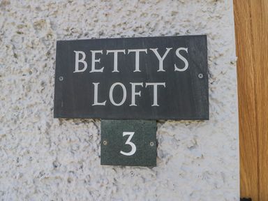 A black sign with white letters displaying Bettys Loft and the number 3 on a textured white wall