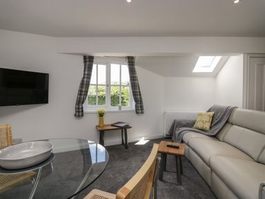 A living room with a glass table chairs a sofa a window with curtains and a wall-mounted TV at Betty's Loft in Hawkshead