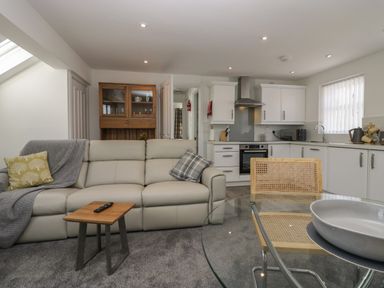 An open plan living area with a sofa, small wooden table, glass dining table with chairs, and a kitchen with white cabinets at Betty's Loft in Hawkshead