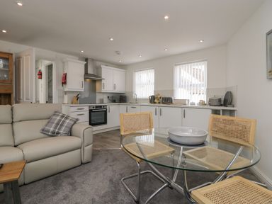 A kitchen and dining area with white cabinets a glass dining table and wooden chairs at Betty's Loft in Hawkshead
