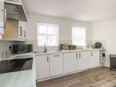 A kitchen with white cabinets a sink microwave toaster kettle and windows at Betty's Loft in Hawkshead