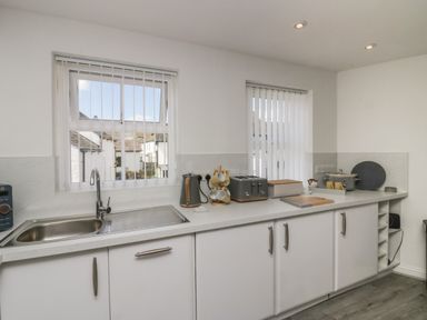 A kitchen with a sink to the left two windows with blinds toaster kettle bread box and storage cabinets at Bettys Loft in Hawkshead